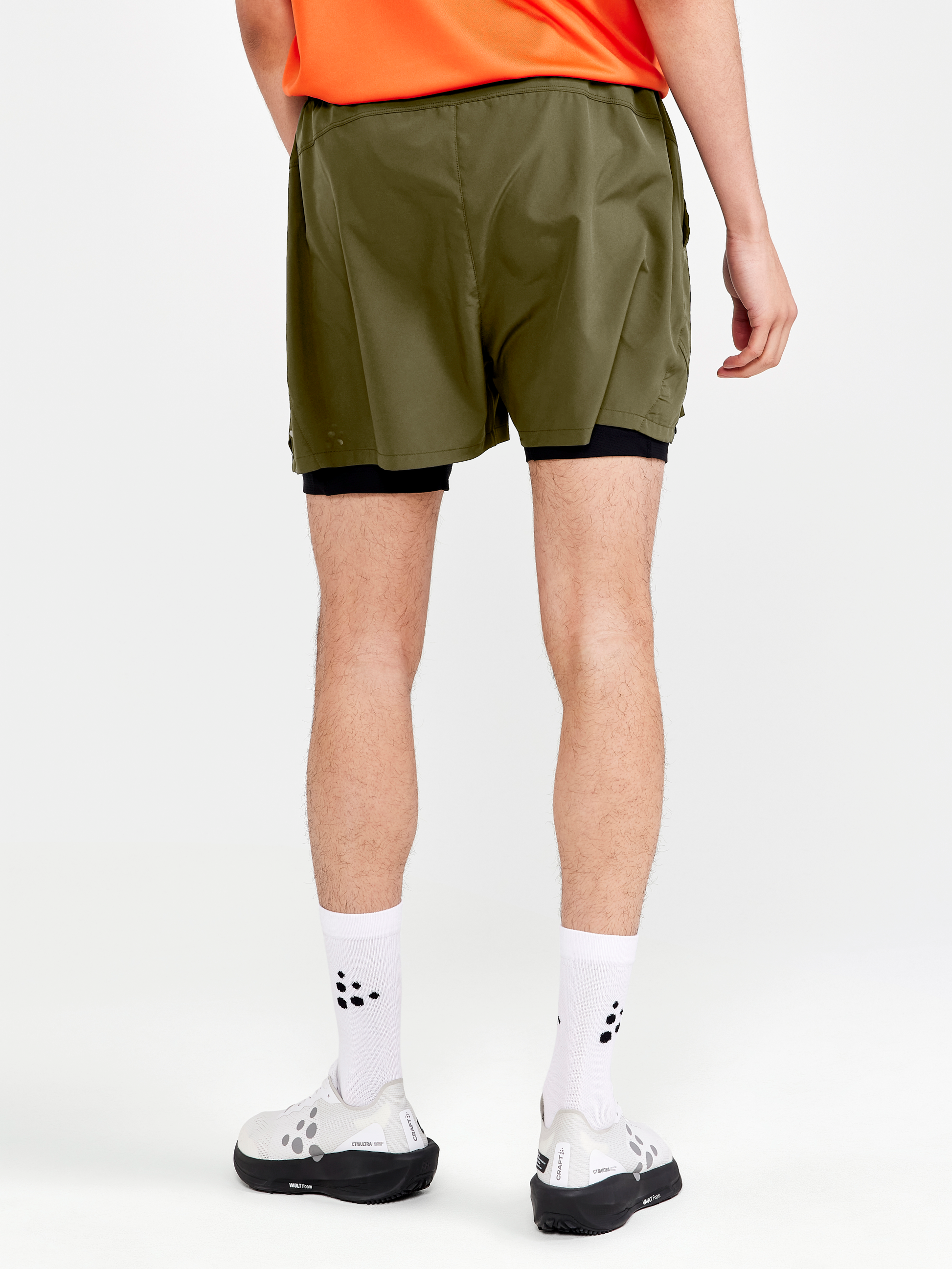 Man models olive green running shorts with built-in liner shorts from the back.