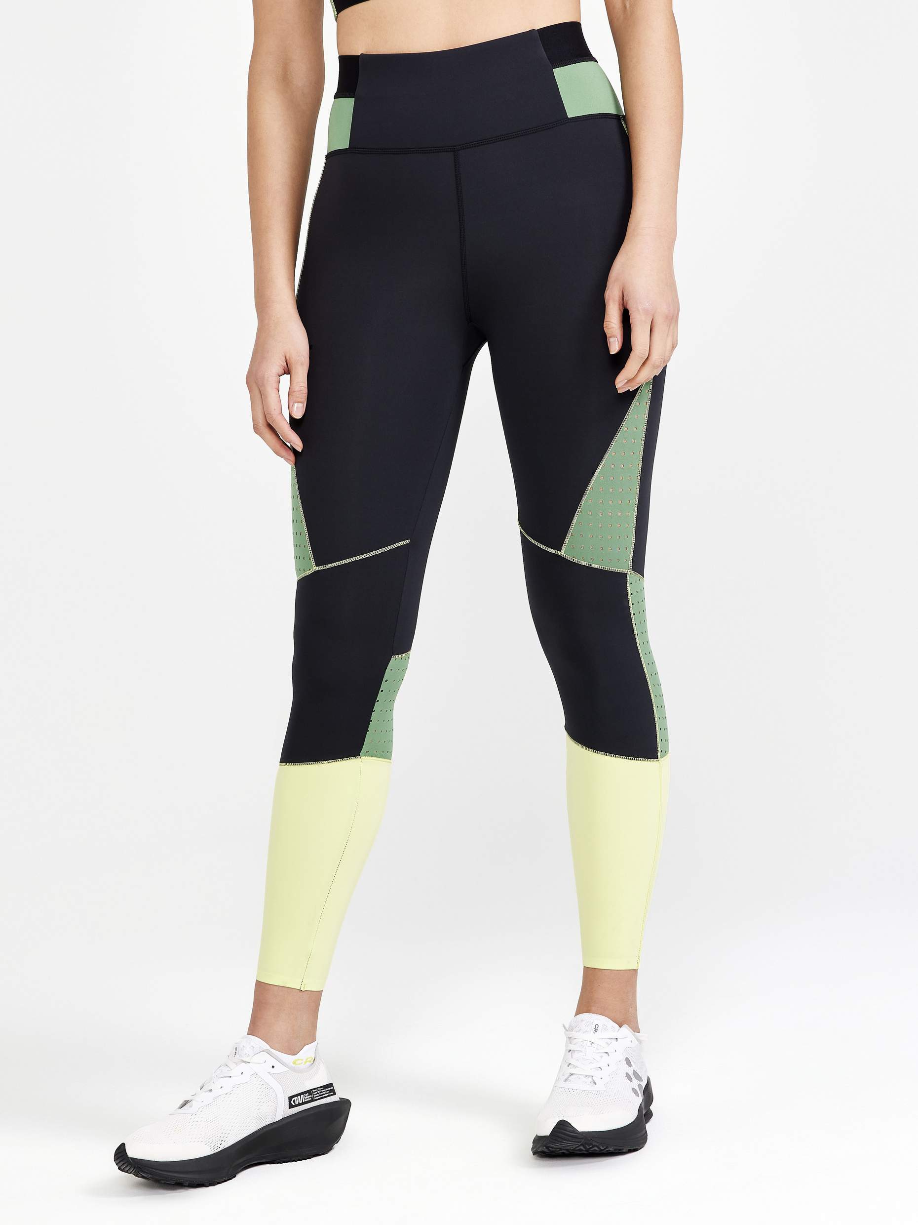 Woman models black and yellow high-waisted workout leggings with green side panels featuring breathable cutouts.