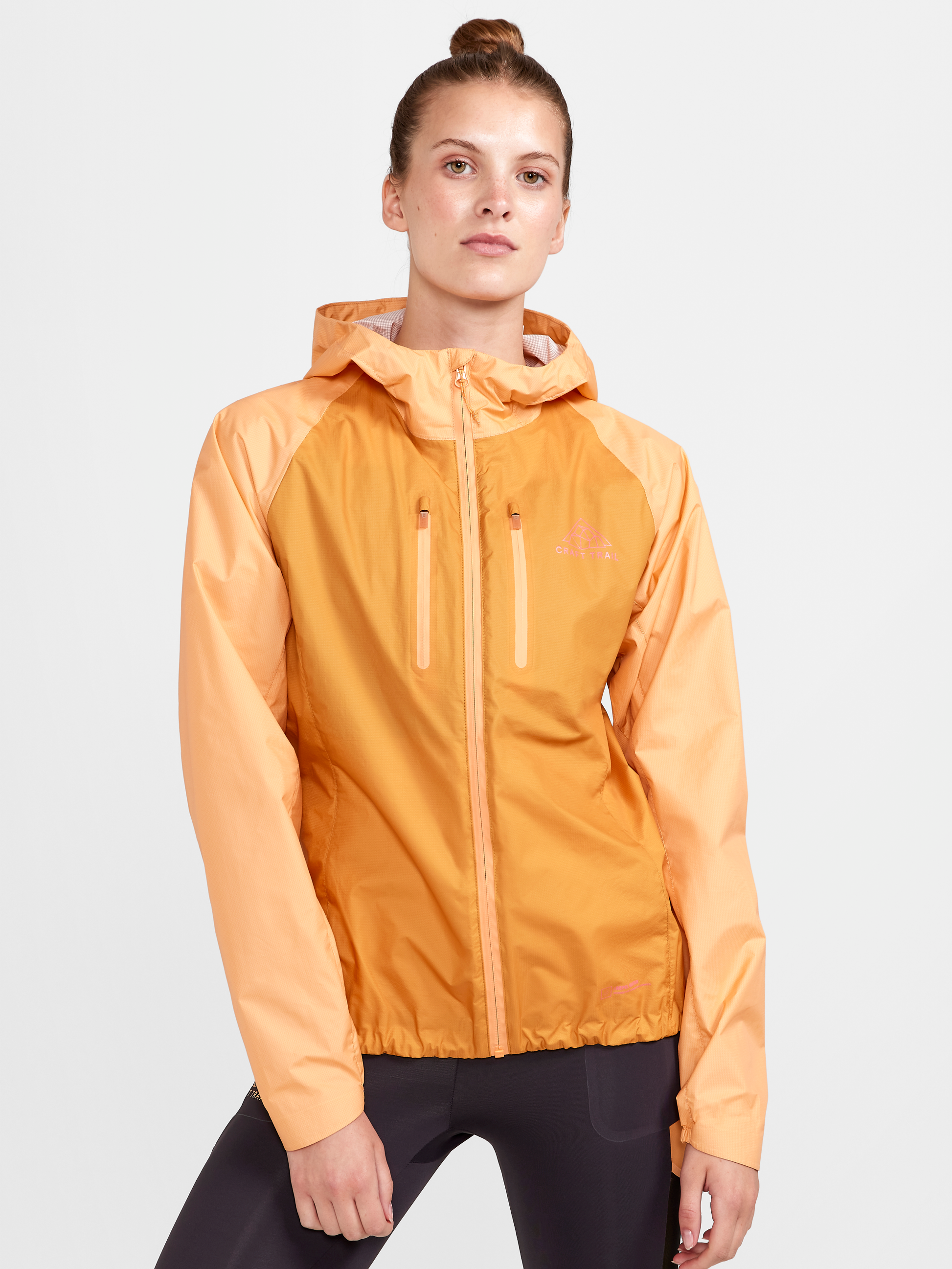 Woman models a lightweight, peach-colored rain jacket with a hood and zippered pockets.