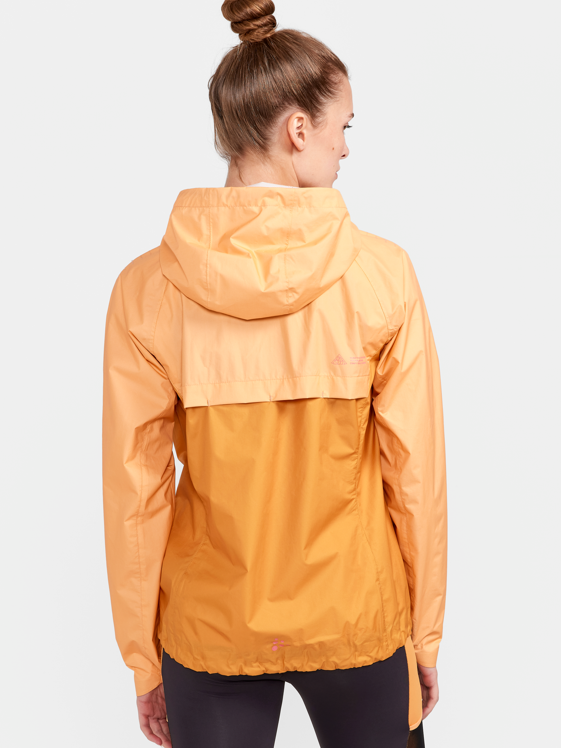 Woman models a lightweight, packable orange rain jacket with hood.