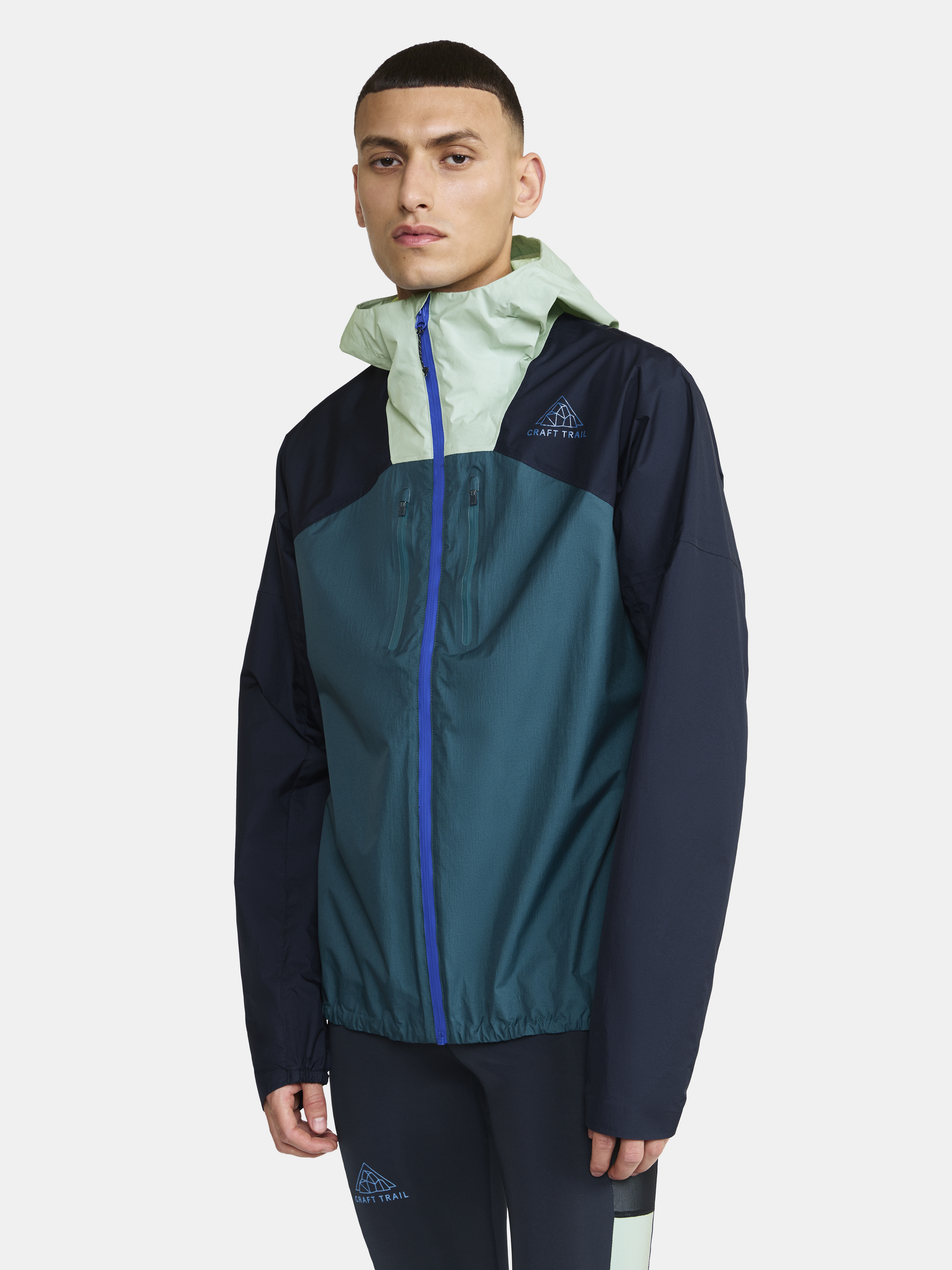 Man wearing a teal and navy blue Craft Trail running jacket with a hood.