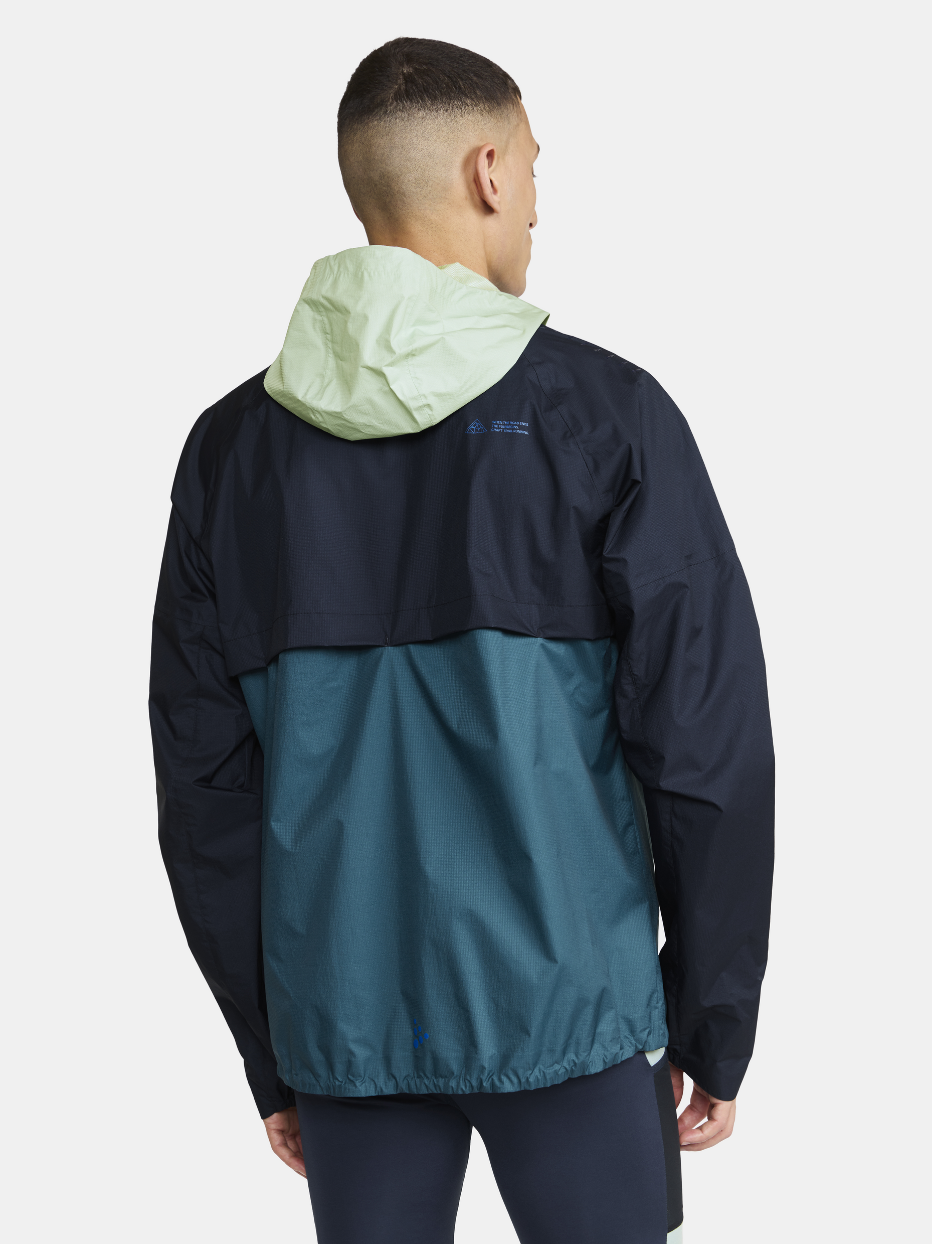Man models a color-blocked teal and black running jacket with a pale green hood, showcasing its back view.