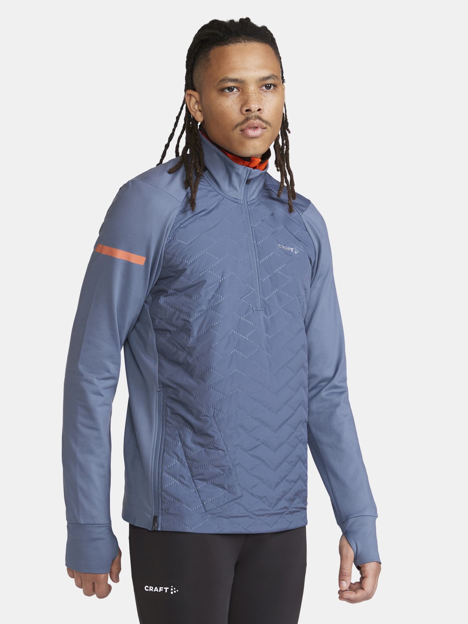 Man models a blue Craft® athletic quarter-zip pullover with chevron quilting and orange accents.