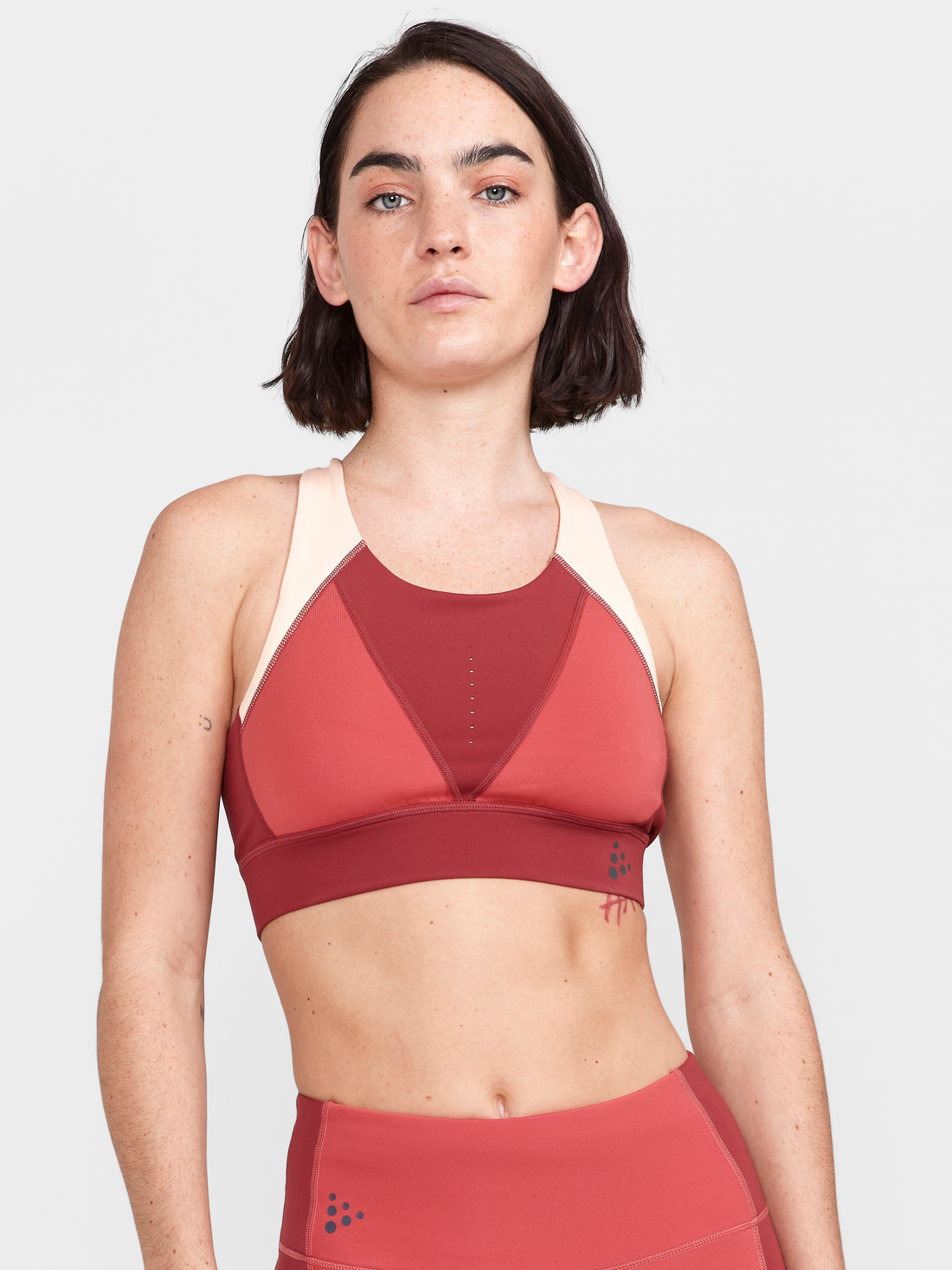 Woman models a maroon and pink athletic sports bra with a racerback design.
