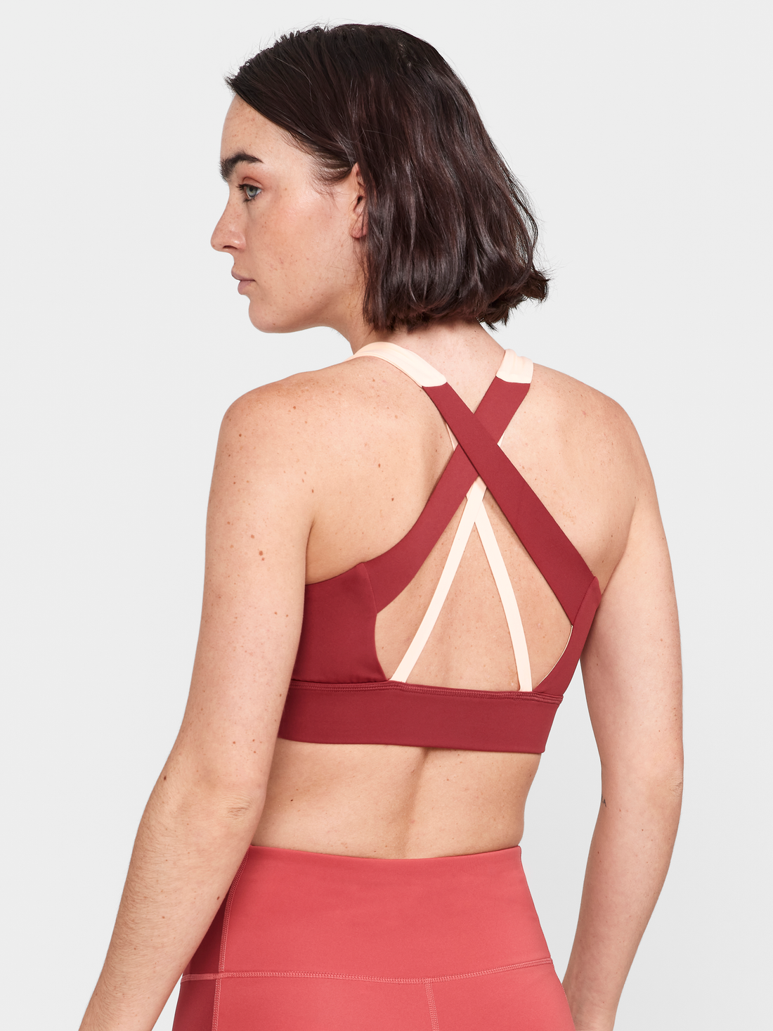 Woman models a maroon and pink athletic sports bra with a racerback design.