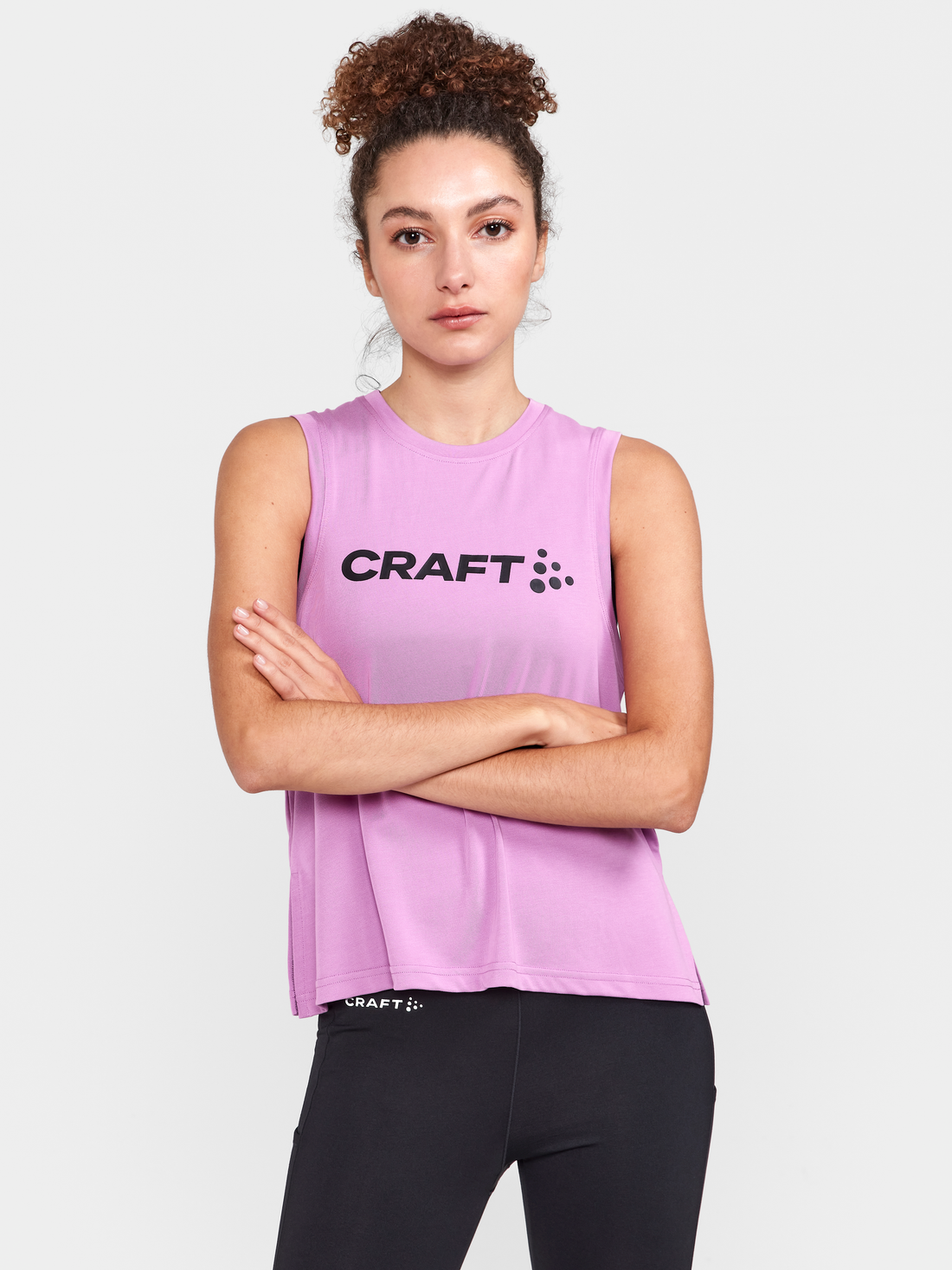Woman models a purple sleeveless Craft athletic shirt with matching black leggings.