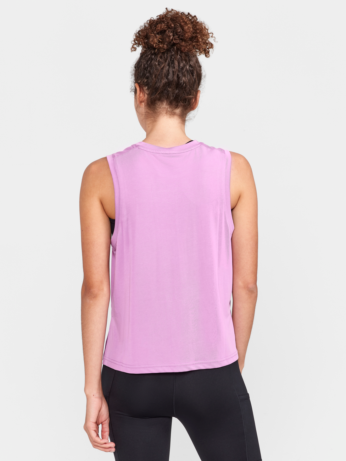 Woman models a purple sleeveless Craft athletic shirt with matching black leggings.