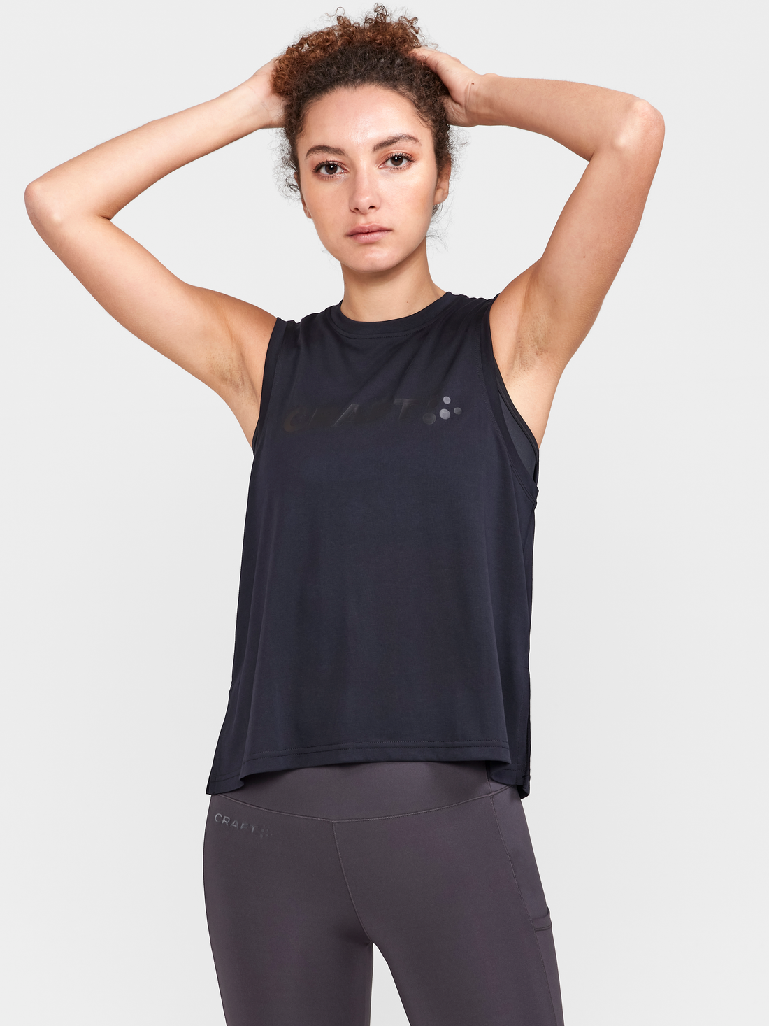 Woman models a black sleeveless athletic shirt and gray leggings, showcasing its breathable design for workouts.