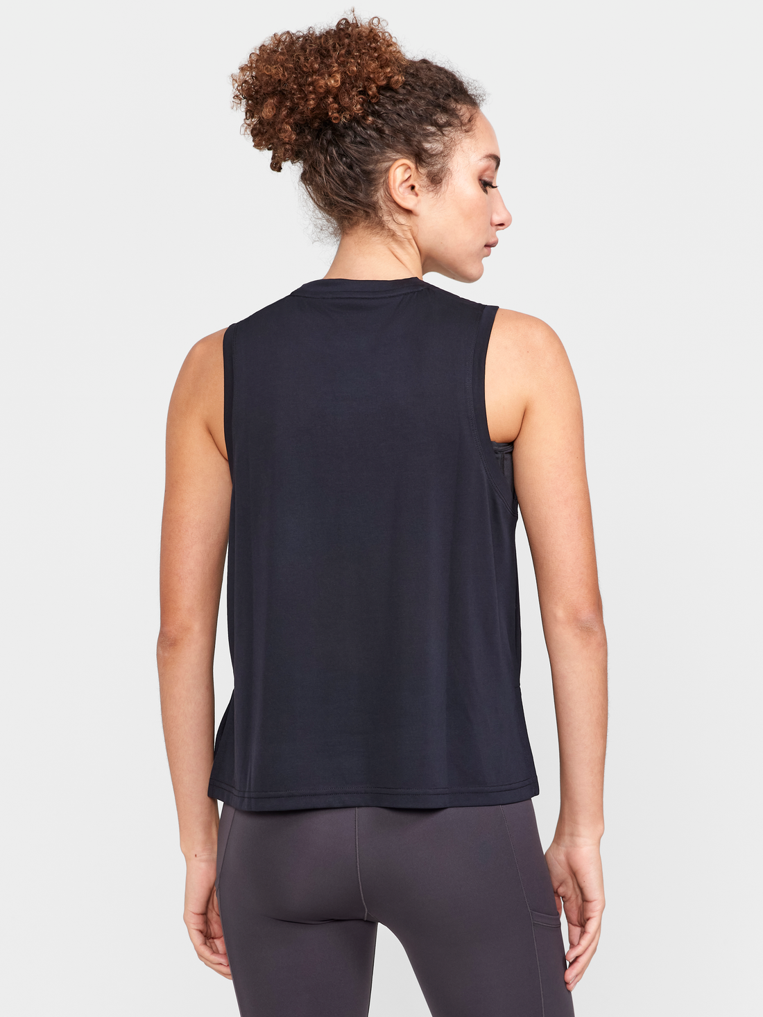 Woman models a black sleeveless athletic shirt and gray leggings, showcasing its breathable design for workouts.