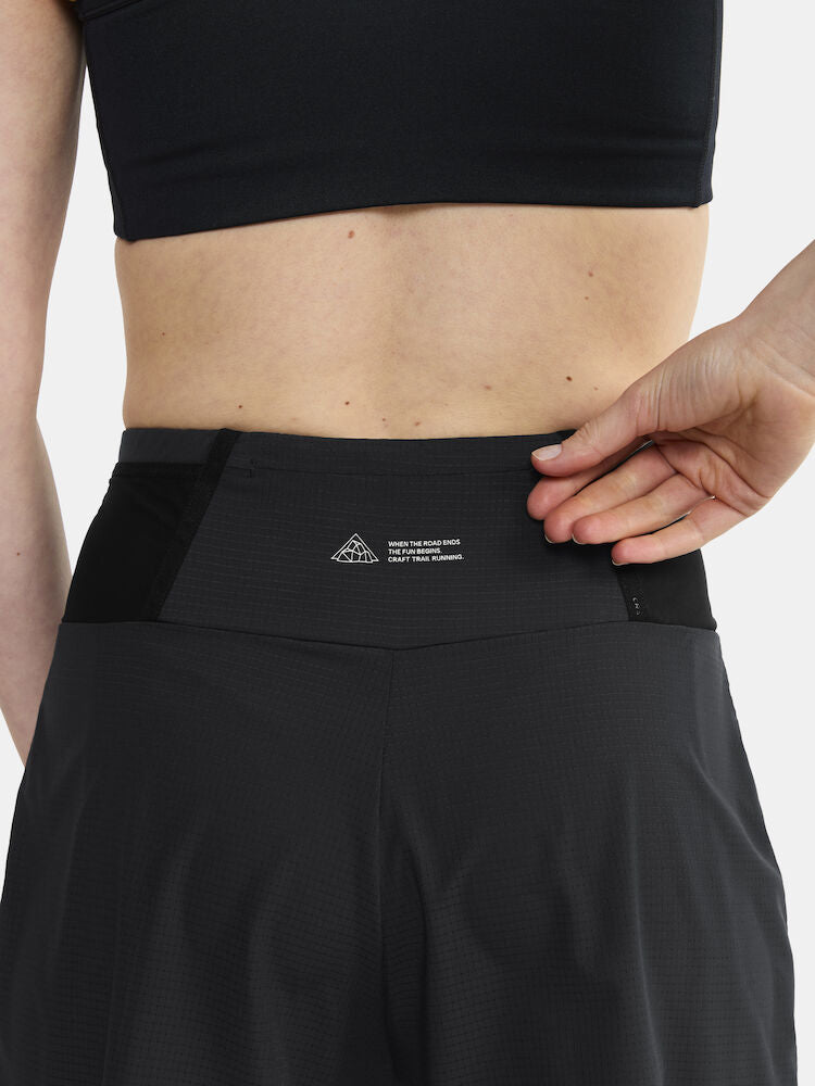 Woman adjusts black athletic shorts with "Where the road ends, the fun begins" printed on waistband.