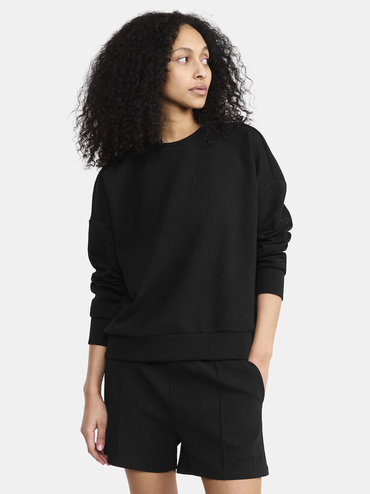 Woman models a black crewneck sweatshirt and matching shorts, showcasing a comfortable and stylish athleisure outfit.