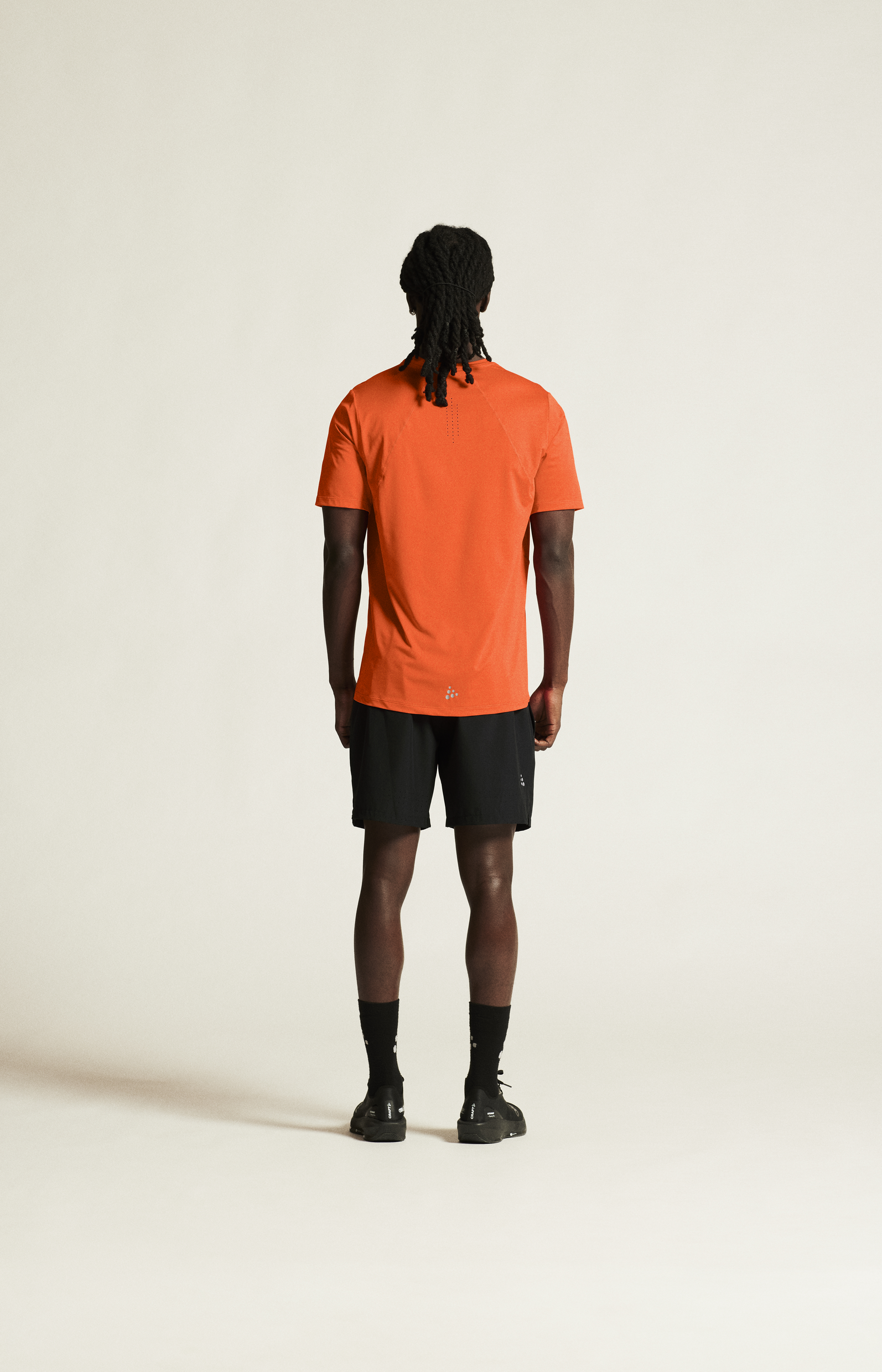 Man models an athletic outfit featuring a bright orange t-shirt and black running shorts from the back.