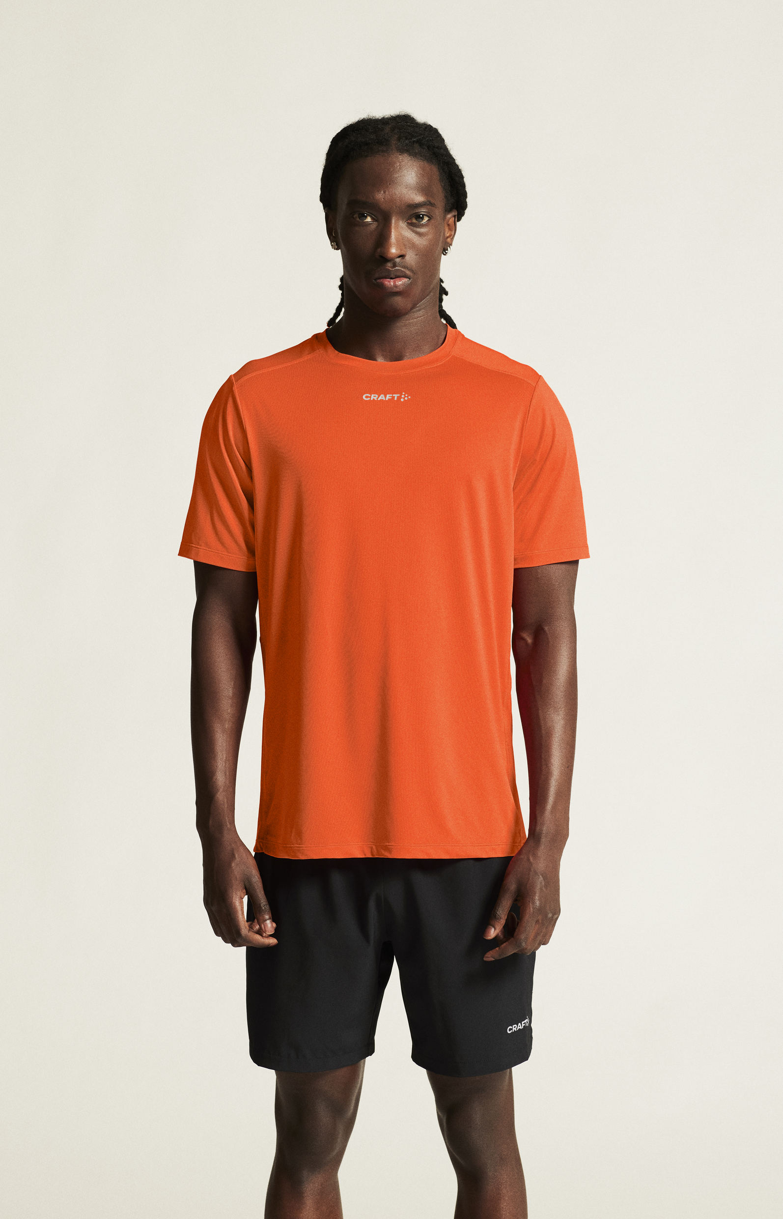 Man models a bright orange Craft® athletic T-shirt and black running shorts.