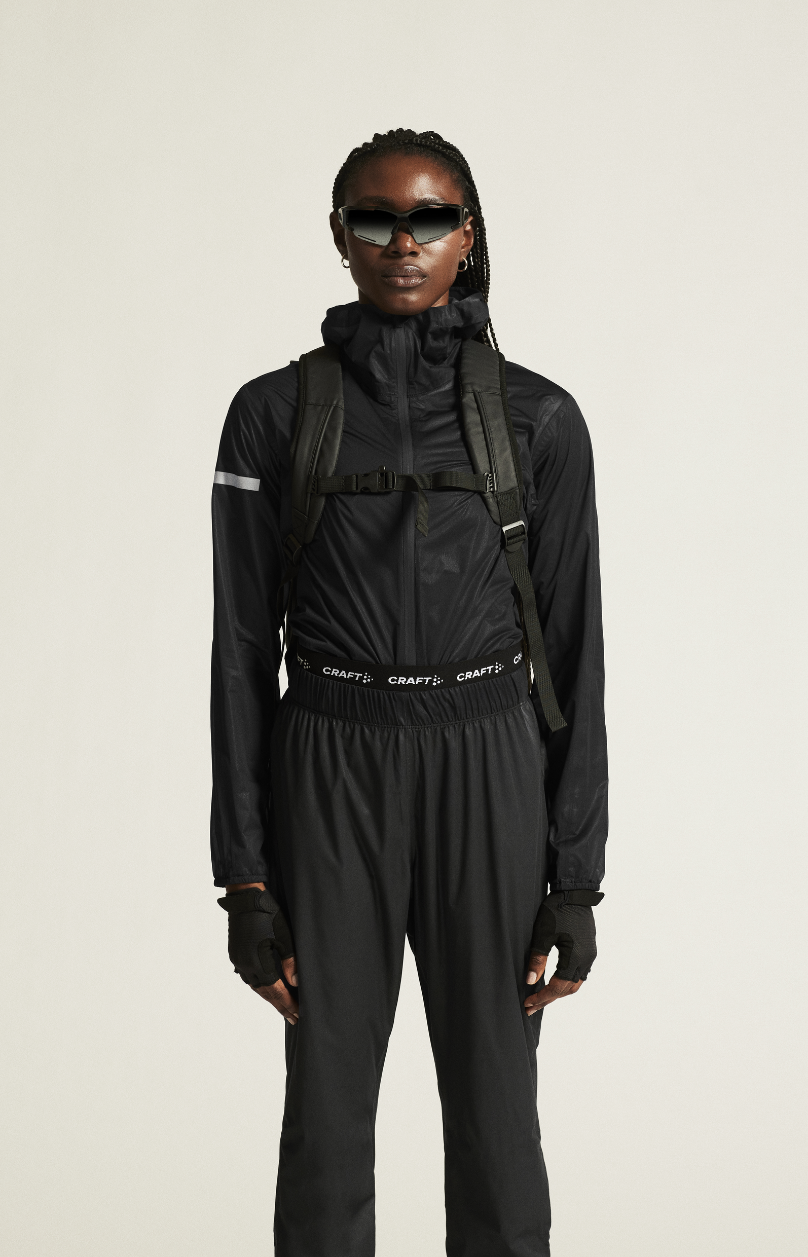 Woman models black weatherproof cycling jacket, pants, and backpack, highlighting activewear for outdoor adventures.