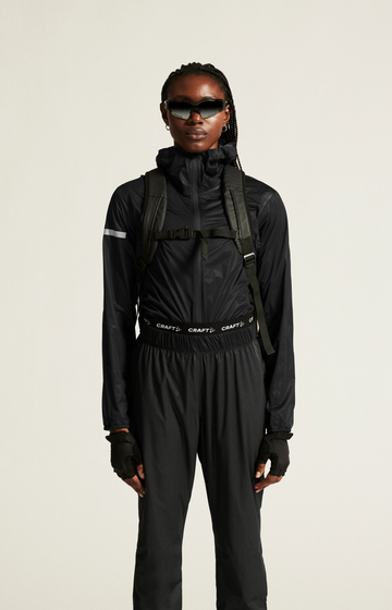 Woman models black weatherproof cycling jacket, pants, and backpack, highlighting activewear for outdoor adventures.