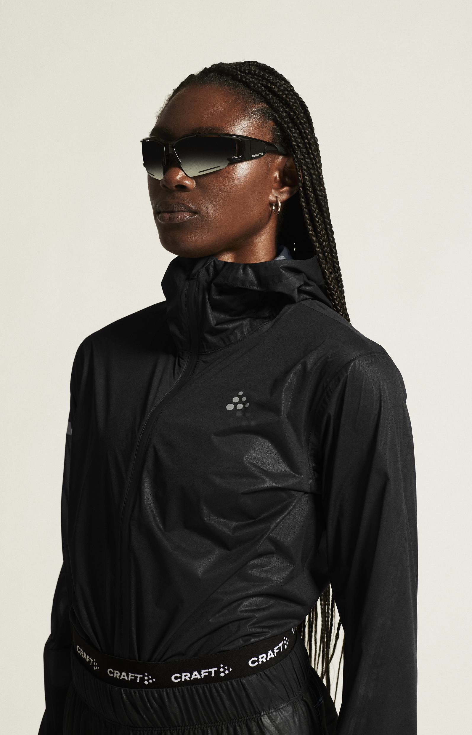 Woman wears black athletic sunglasses and a black athletic jacket.