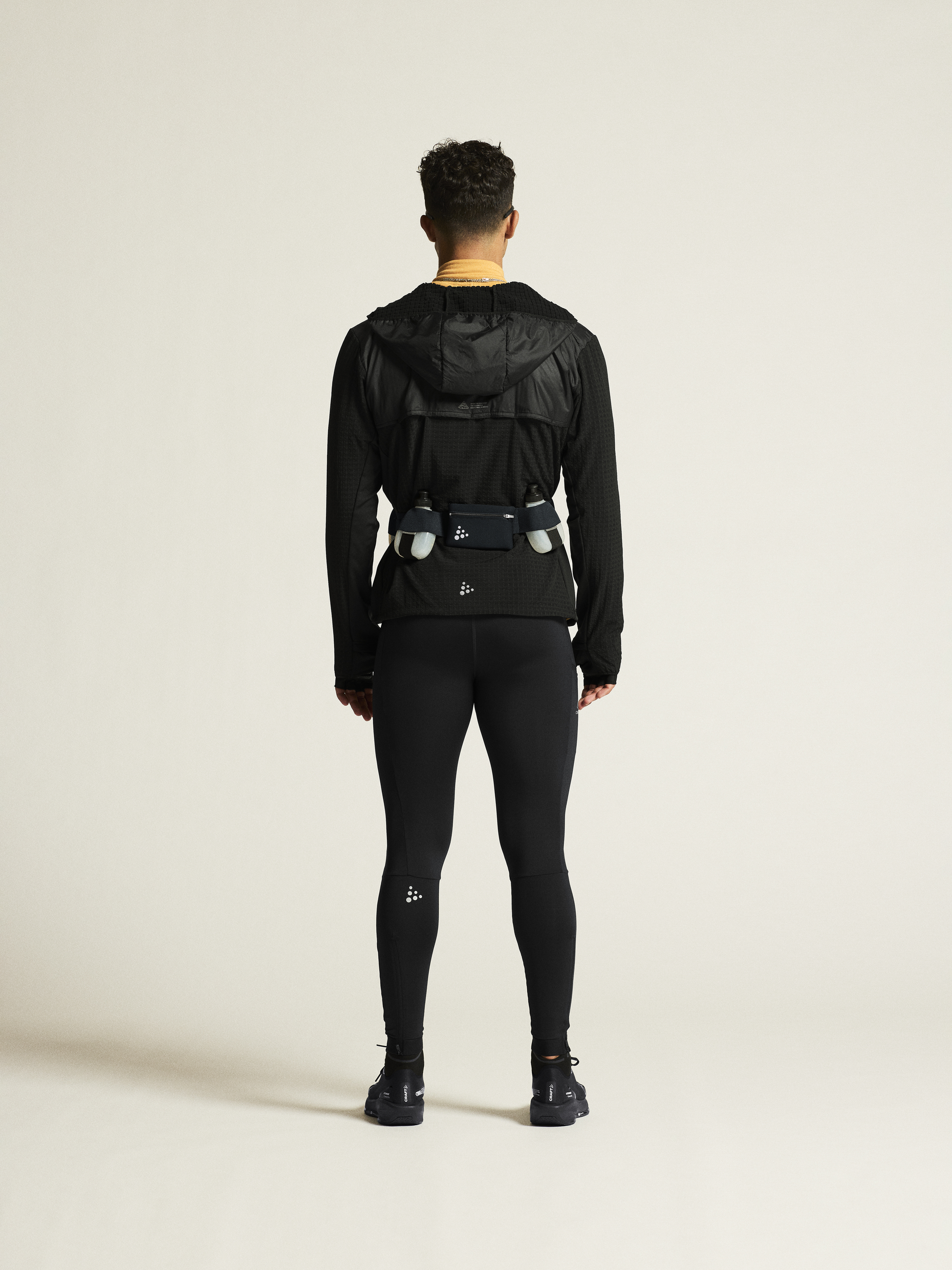 Runner wears black running tights, black hooded jacket, and a black hydration belt with two water bottles.