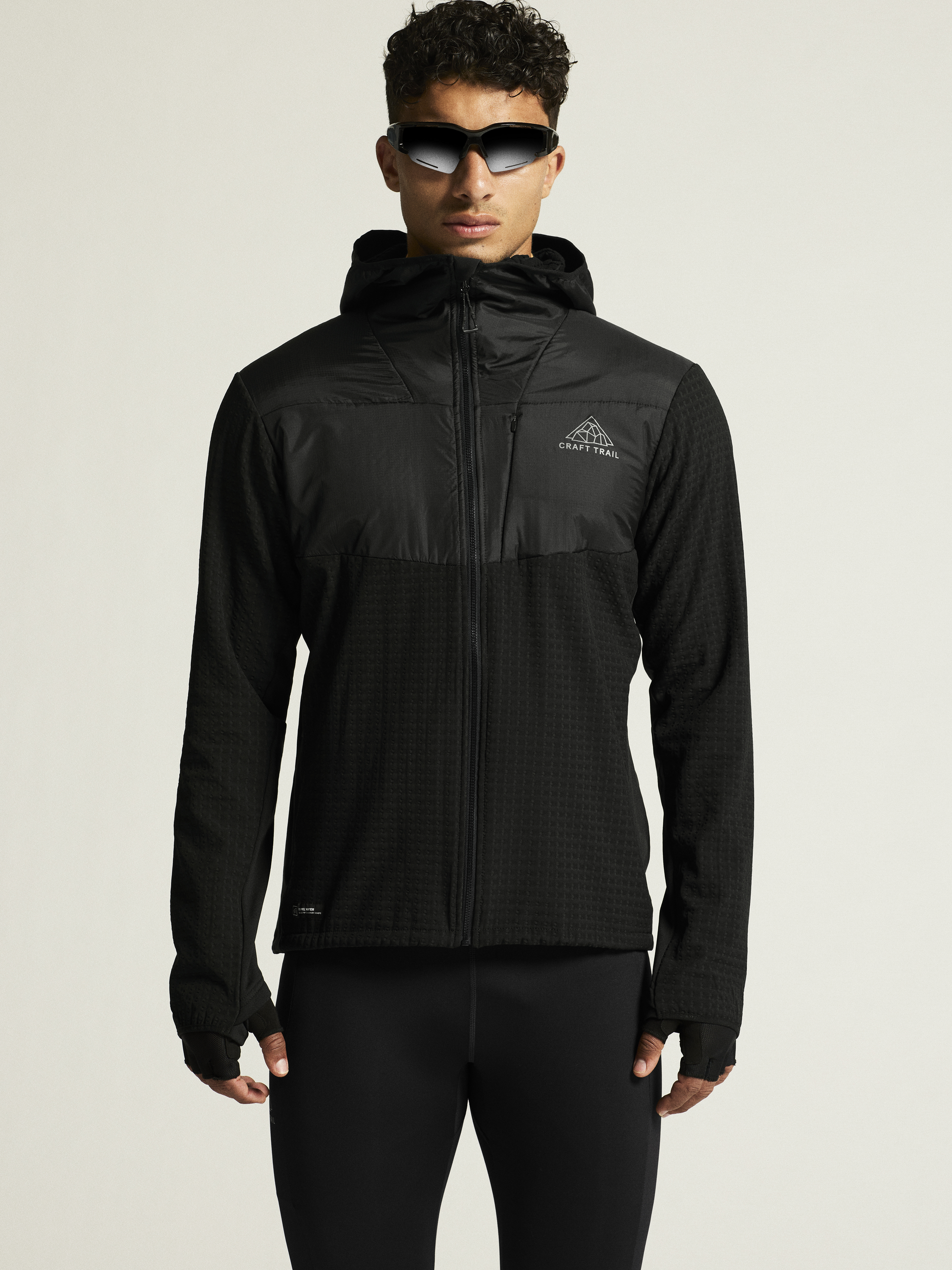 Man models a black hooded running jacket with thumbholes and a chest logo.