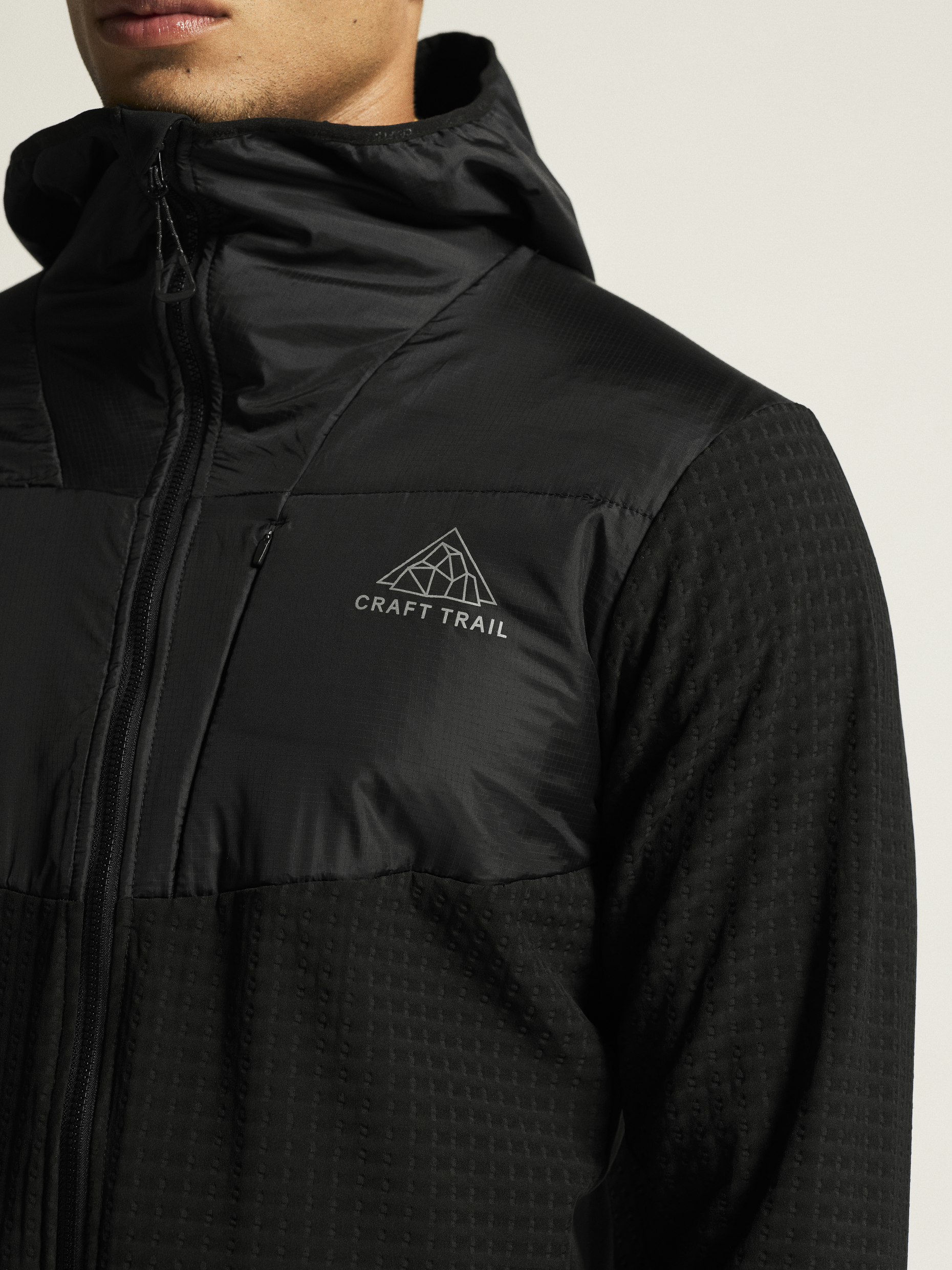 Man wearing a black Craft Trail hooded running jacket with a zippered front.