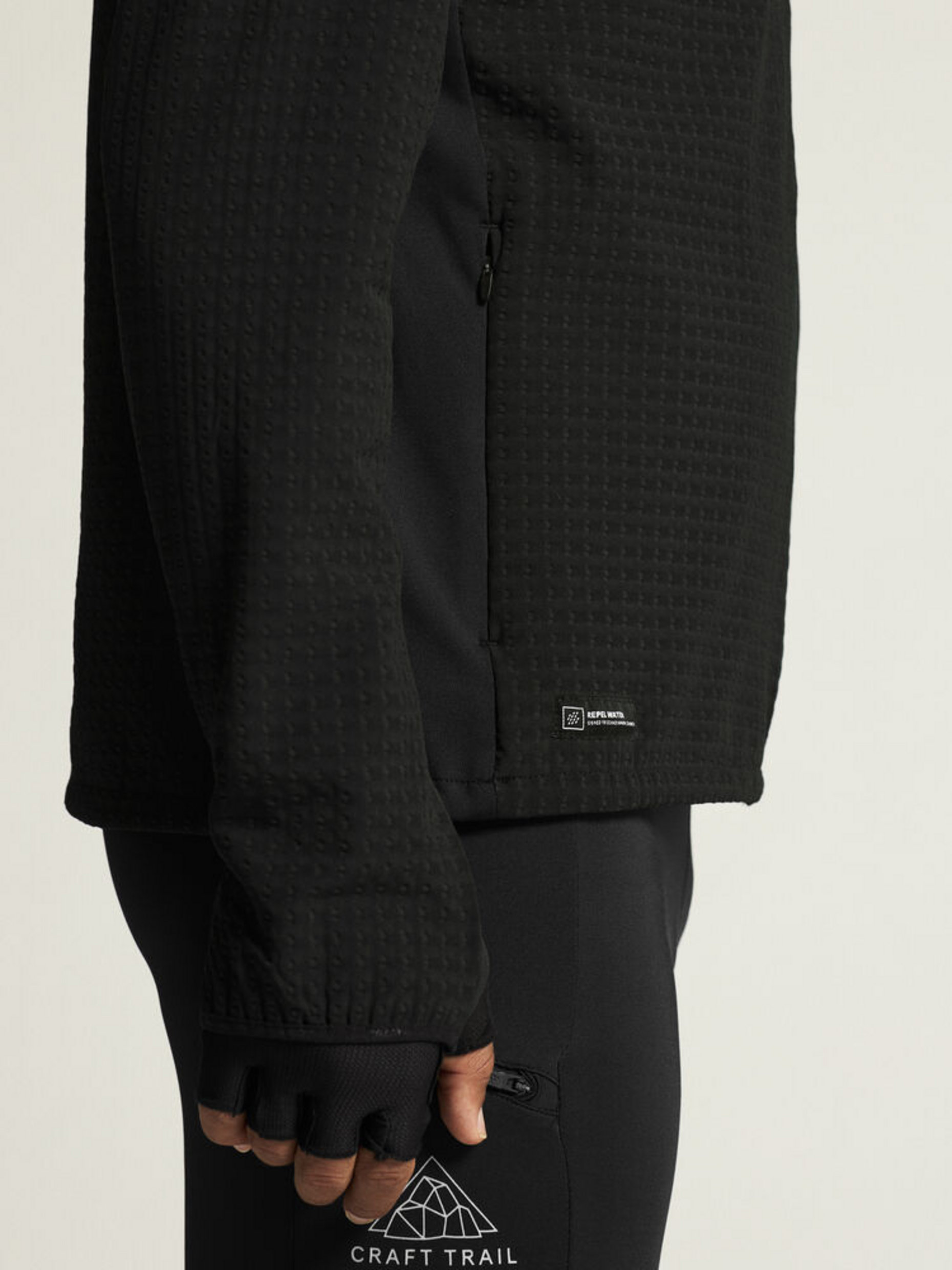 Man wearing a black running jacket with a textured pattern and zippered pocket.