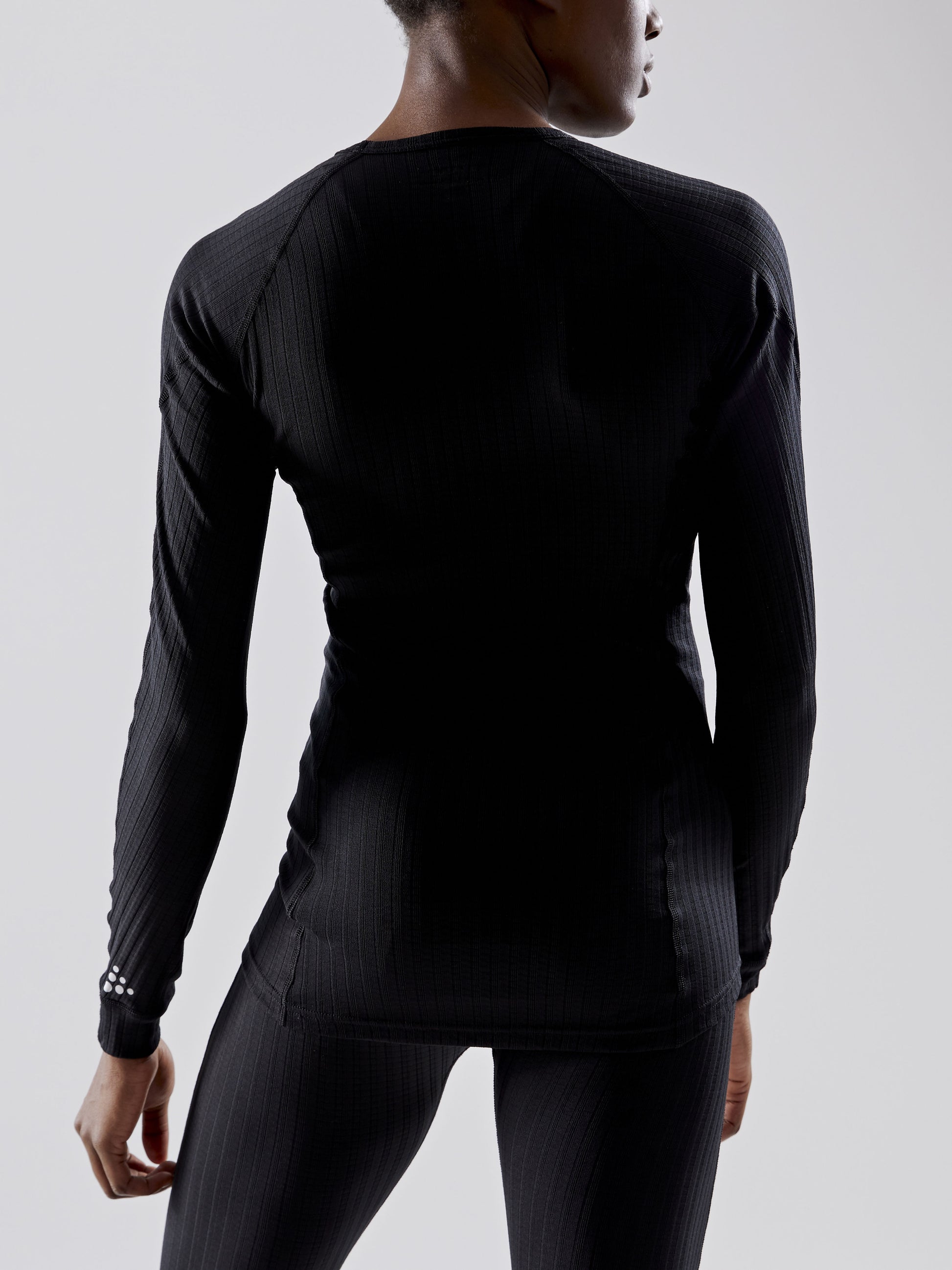 Woman models black ribbed thermal base layer shirt from the back.