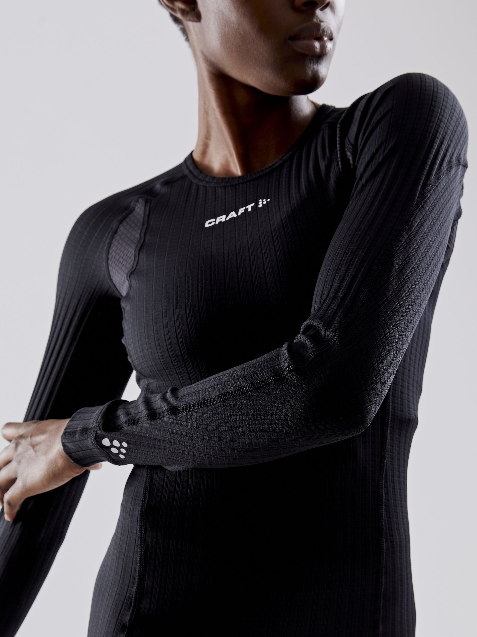 Woman models a black, long-sleeved athletic undershirt with textured fabric.