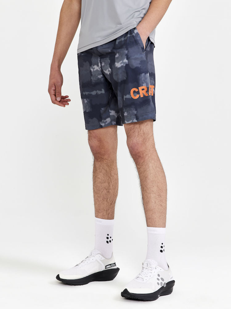 Man models gray abstract-patterned athletic shorts with orange "Craft" logo on the right leg.