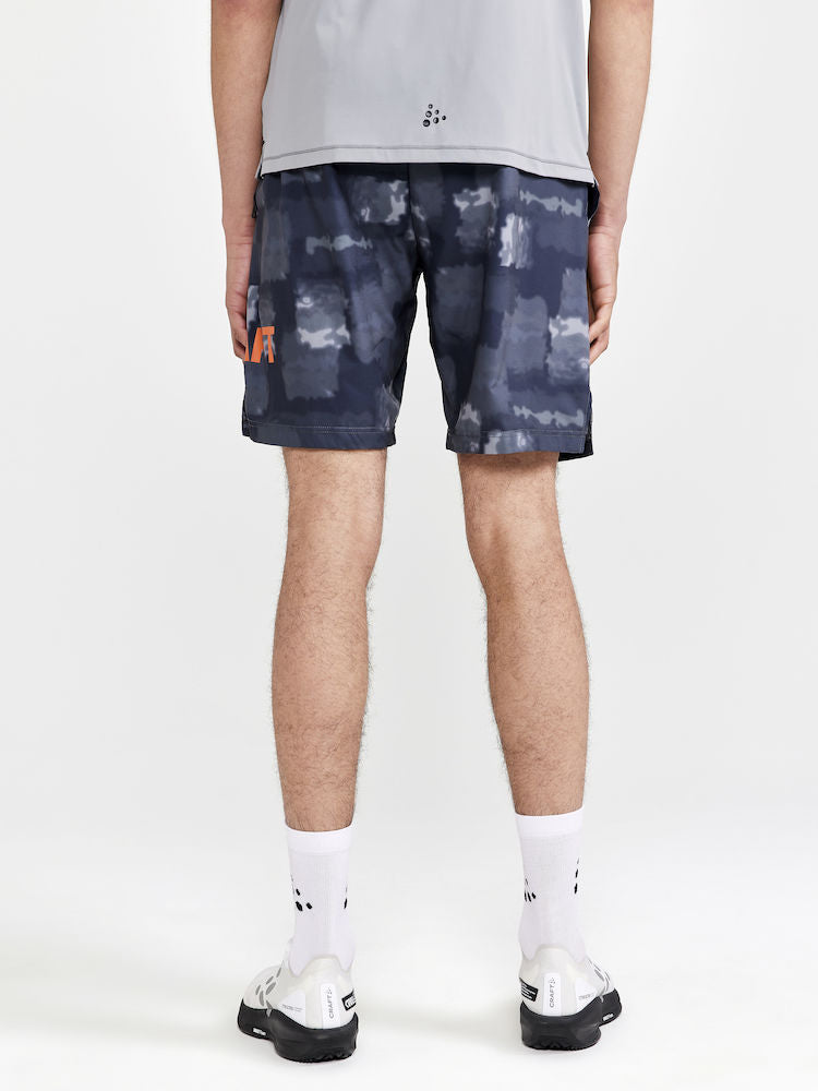 Man models black athletic shorts with abstract print and orange logo, showcasing back view.