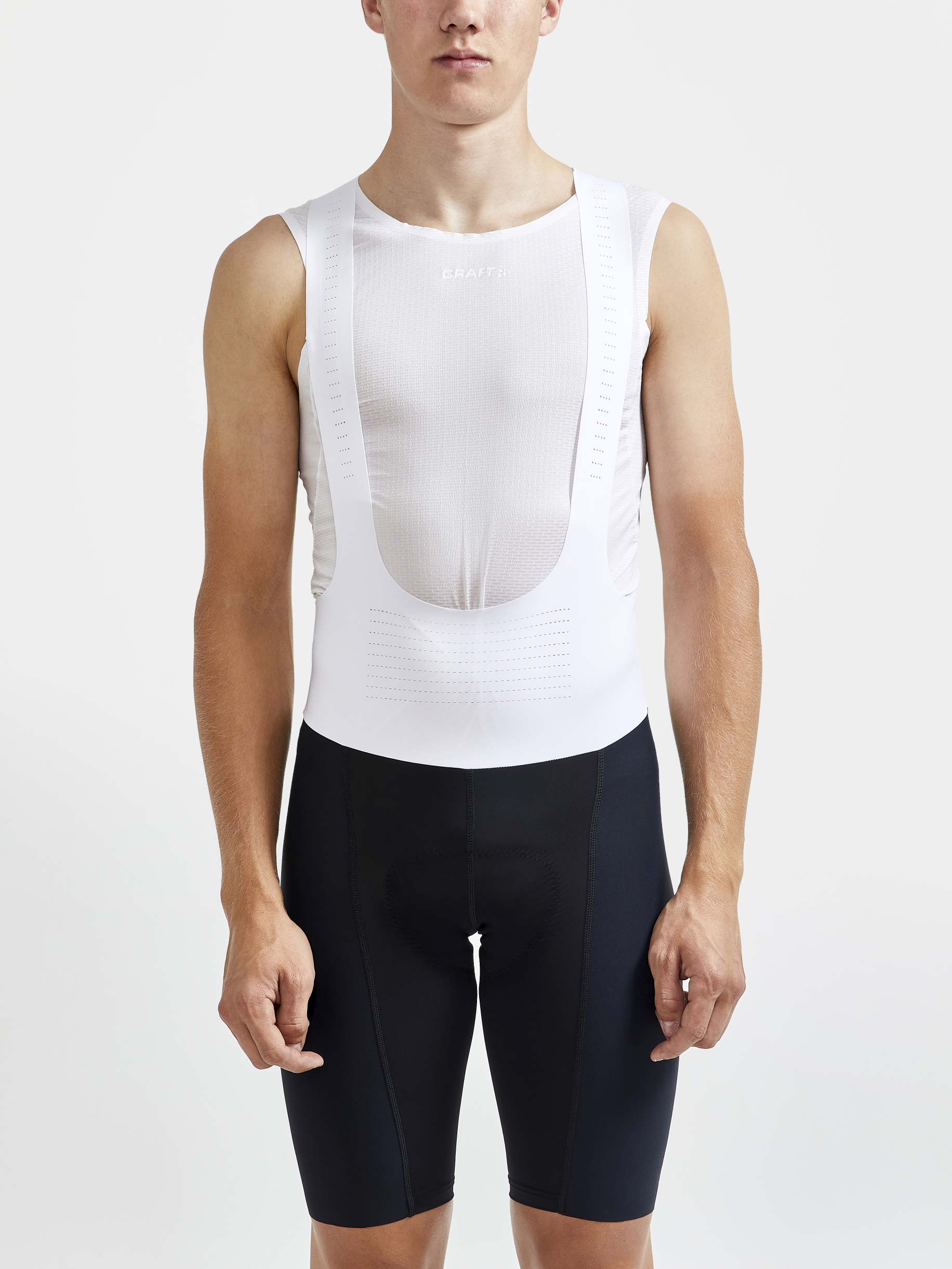 Man models black cycling bib shorts and a white sleeveless base layer.