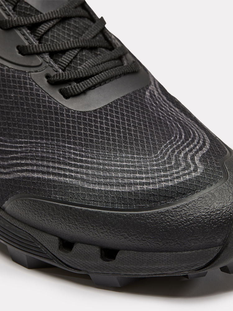 Black trail running shoe showcases breathable mesh upper with textured pattern and rugged outsole for grip.