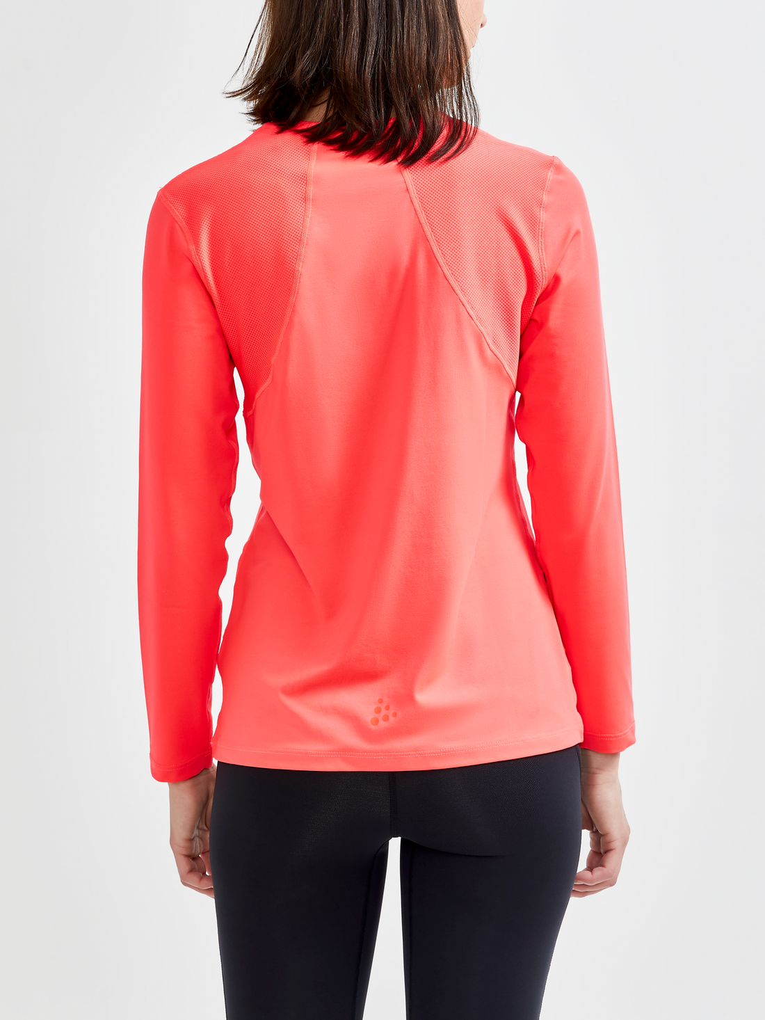 Woman models a bright coral long-sleeve athletic shirt with breathable mesh panels on the shoulders and sides. 
