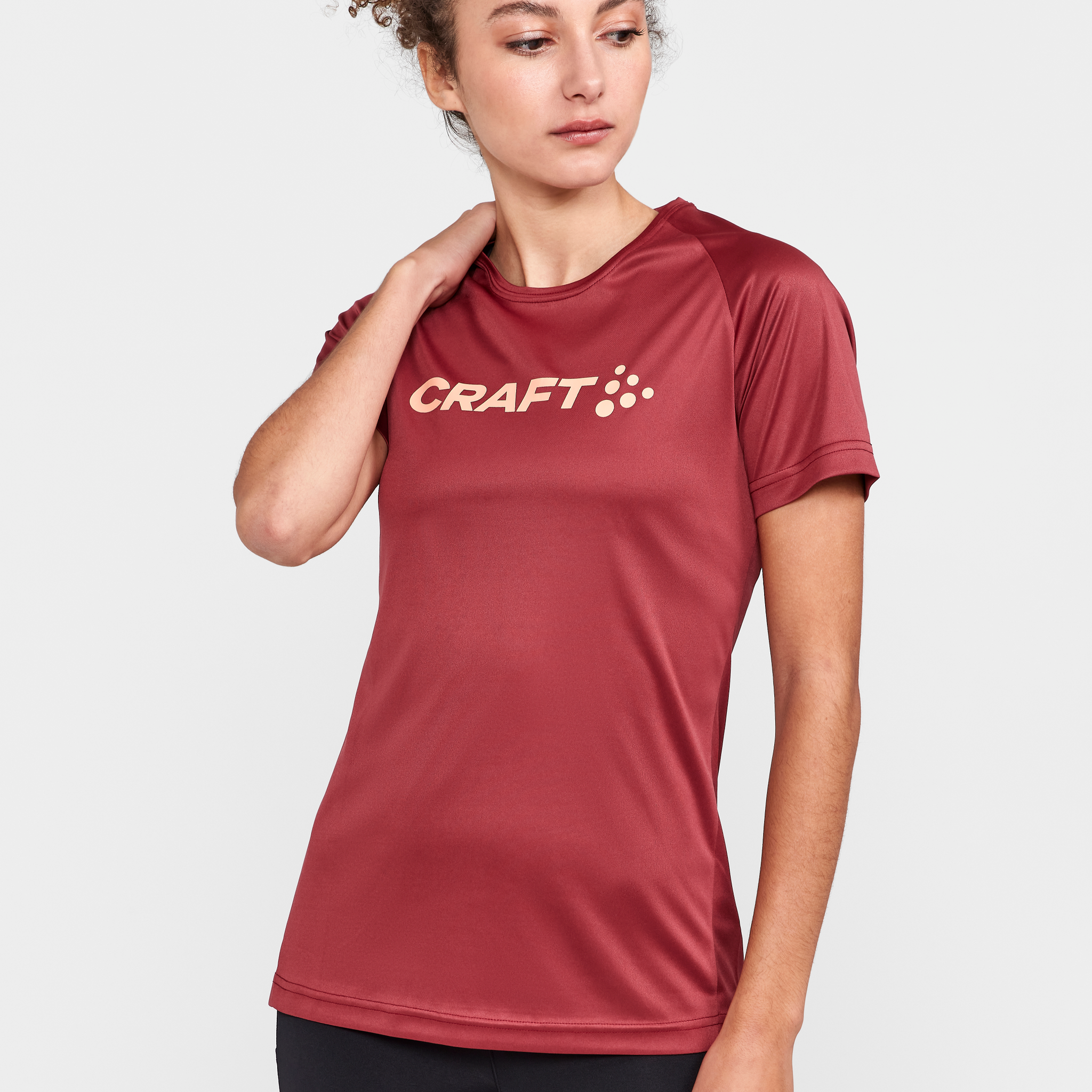 Woman models a maroon athletic t-shirt with the Craft logo on the chest. 
