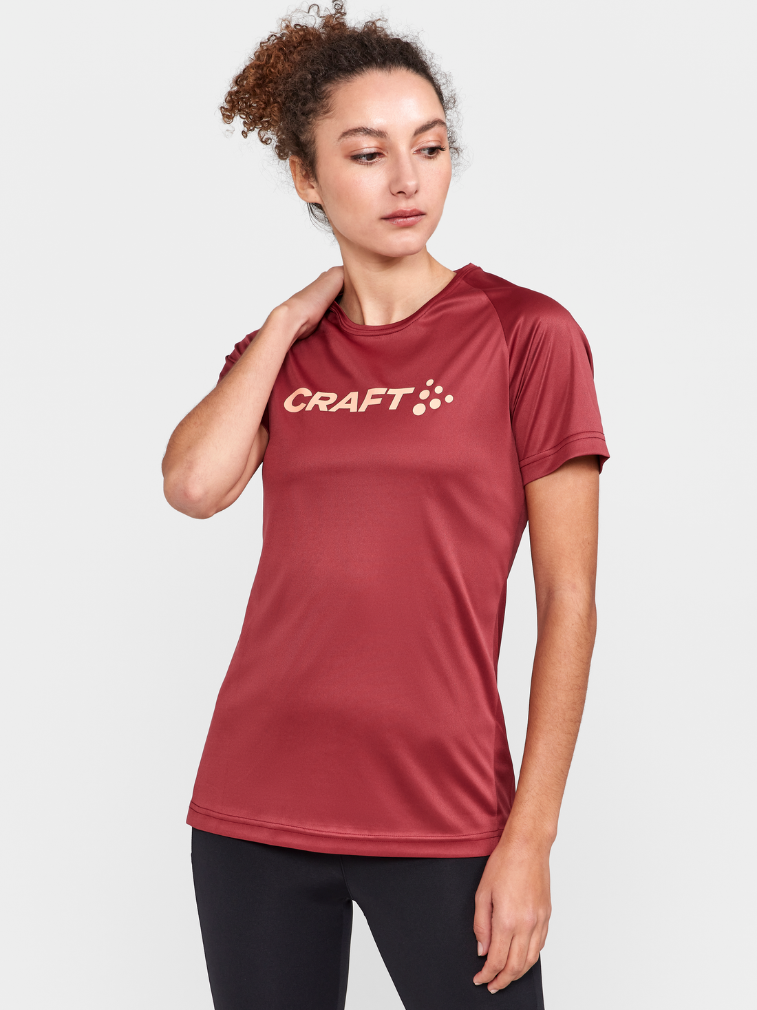 Woman models a maroon athletic t-shirt with the Craft logo on the chest. 
