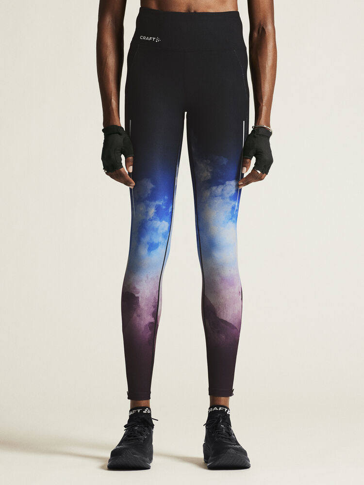 Woman models black Craft high-waisted running leggings with blue and purple ombre cloud design. 
