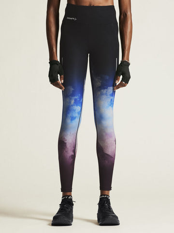 Woman models black Craft high-waisted running leggings with blue and purple ombre cloud design. 
