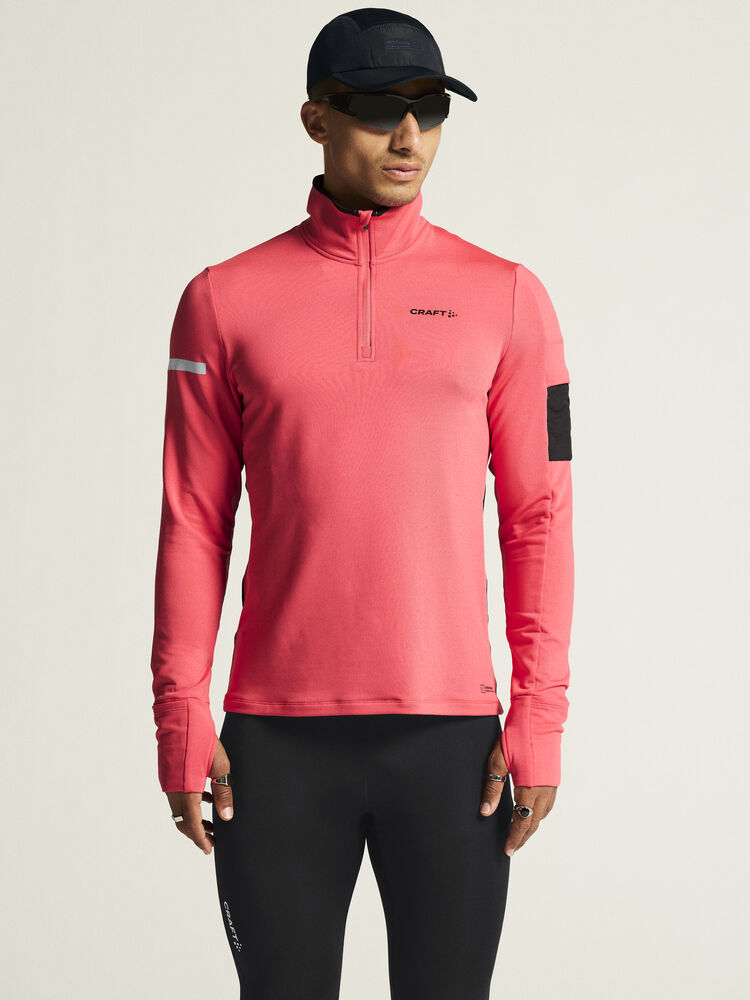 Man models a coral pink Craft Sportswear quarter-zip running top with thumbholes and reflective details. 
