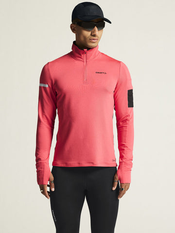 Man models a coral pink Craft Sportswear quarter-zip running top with thumbholes and reflective details. 
