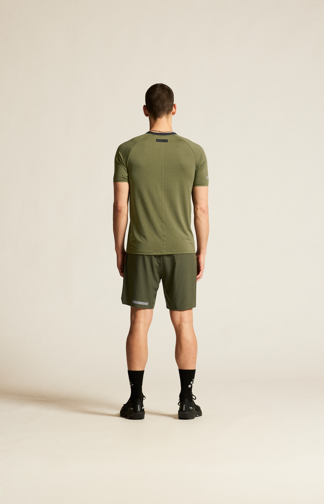 Man models an olive green athletic t-shirt and matching shorts against a beige background. 
