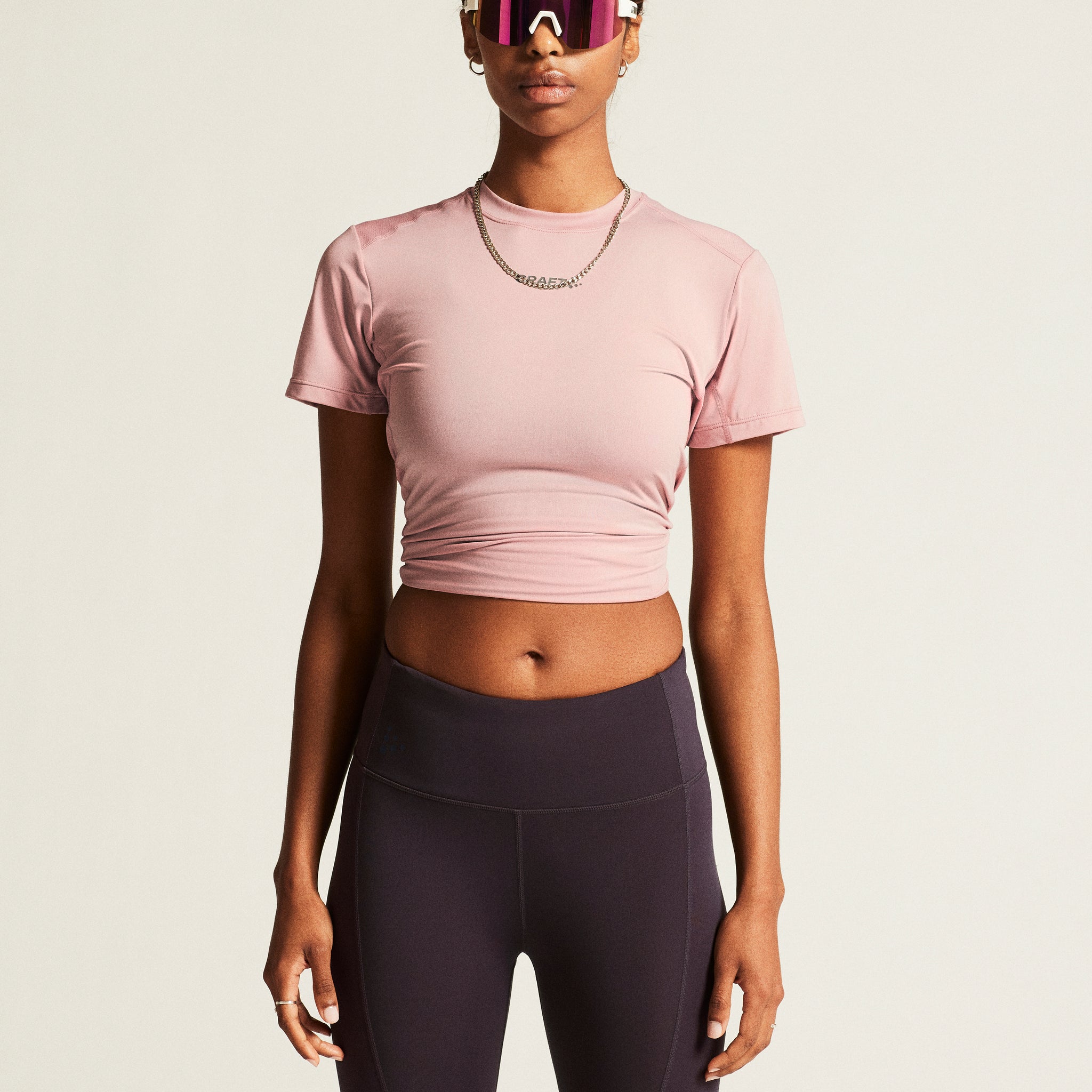 Woman models a dusty pink athletic crop top and dark grey leggings. 
