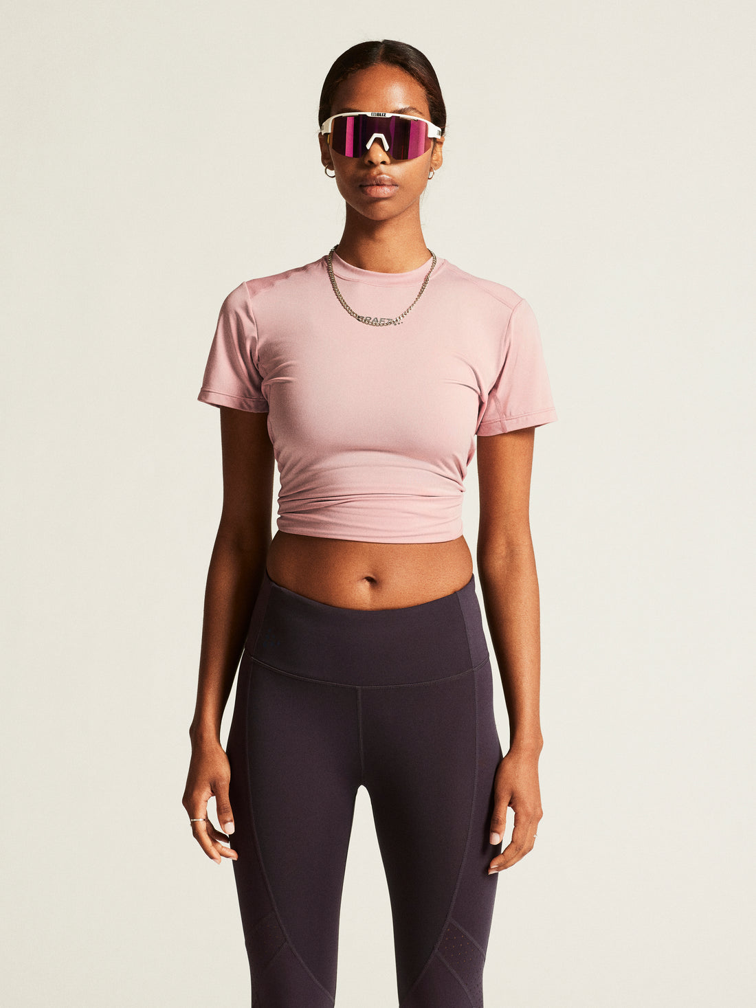 Woman models a dusty pink athletic crop top and dark grey leggings. 
