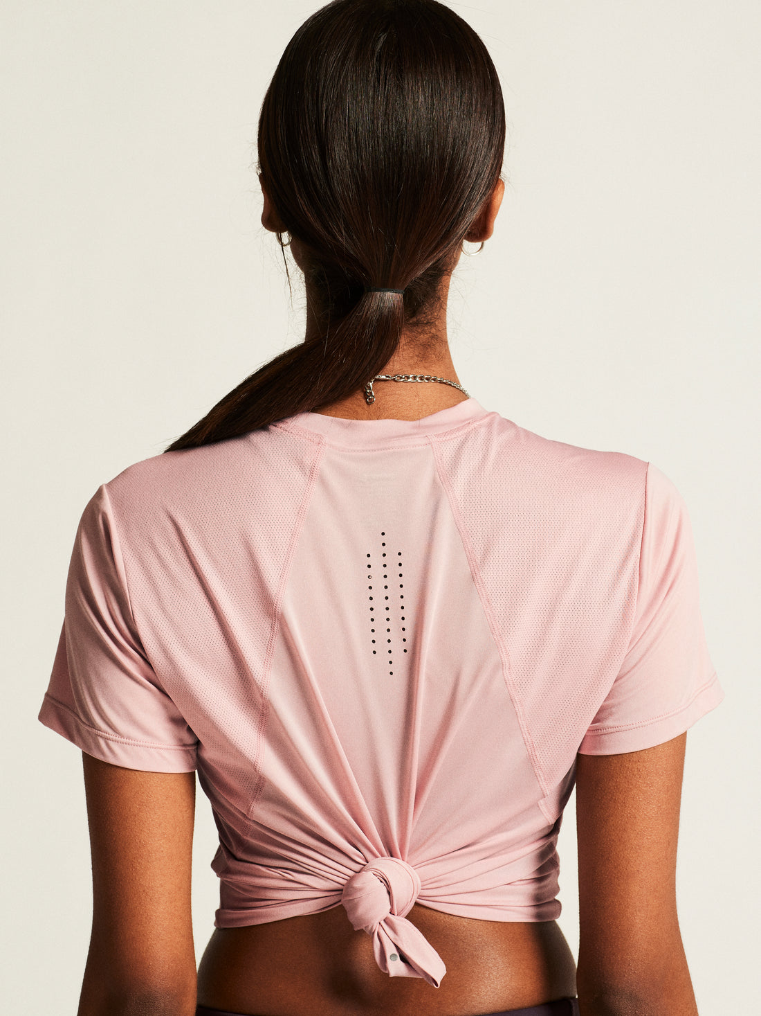 Woman models a dusty pink athletic crop top and dark grey leggings. 
