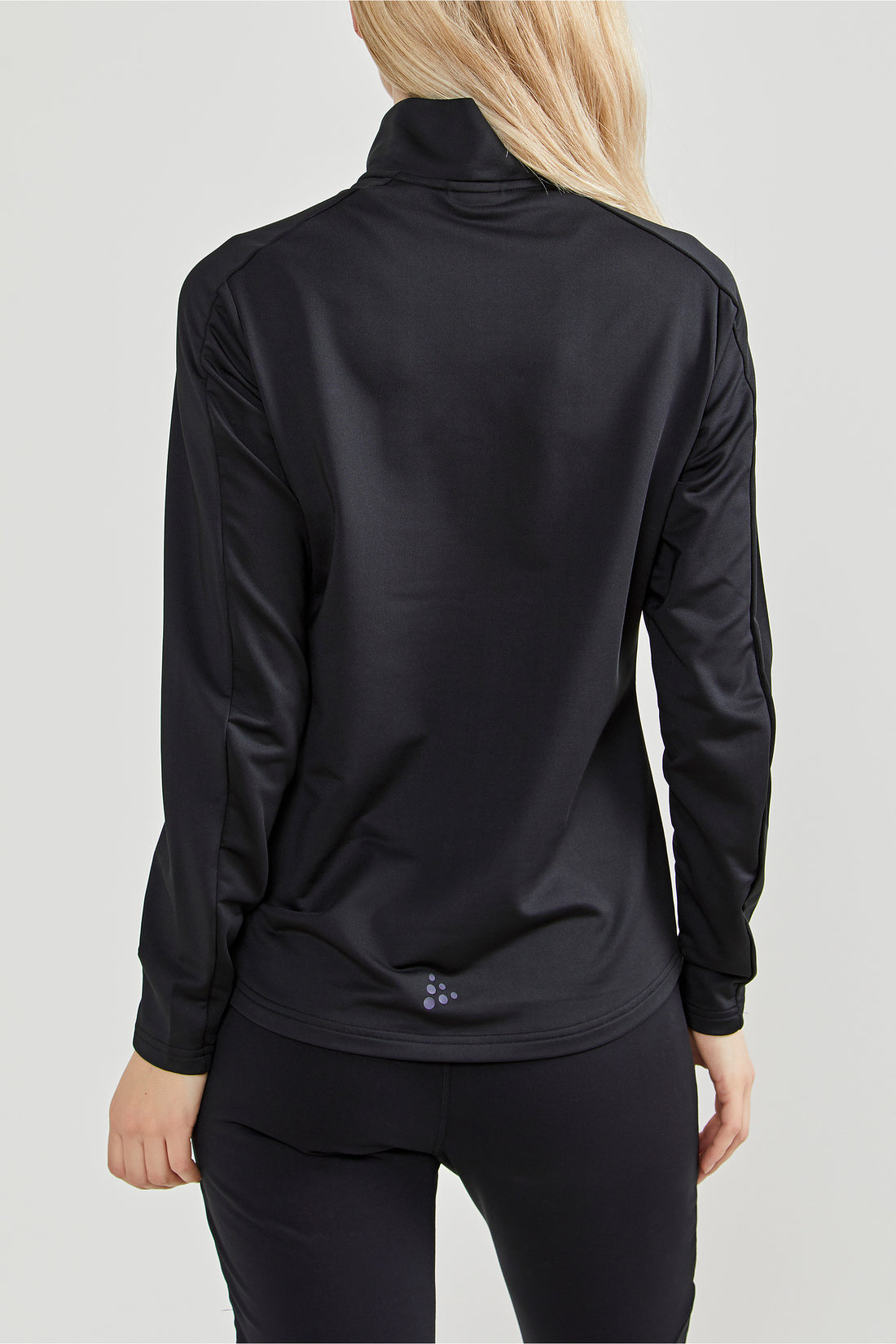 Woman models a black Craft® quarter-zip athletic top with a high collar. 
